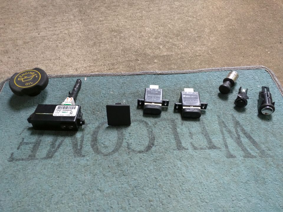 Automotive parts including an engine oil cap, electronic module, and connectors on a teal mat.