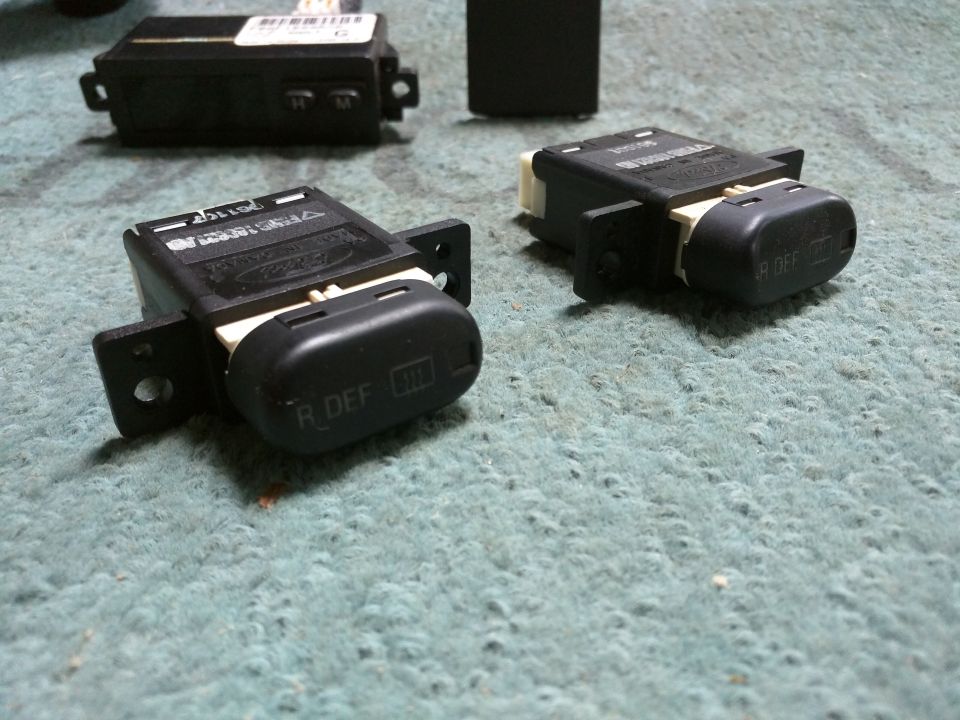 Two black Ford rear window defroster switches on a green surface.
