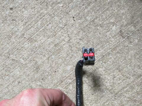 2007 Ford Crown Victoria - A close-up view of a black electrical connector with a red locking tab, attached to a black wire loom. The connector is resting on a textur…