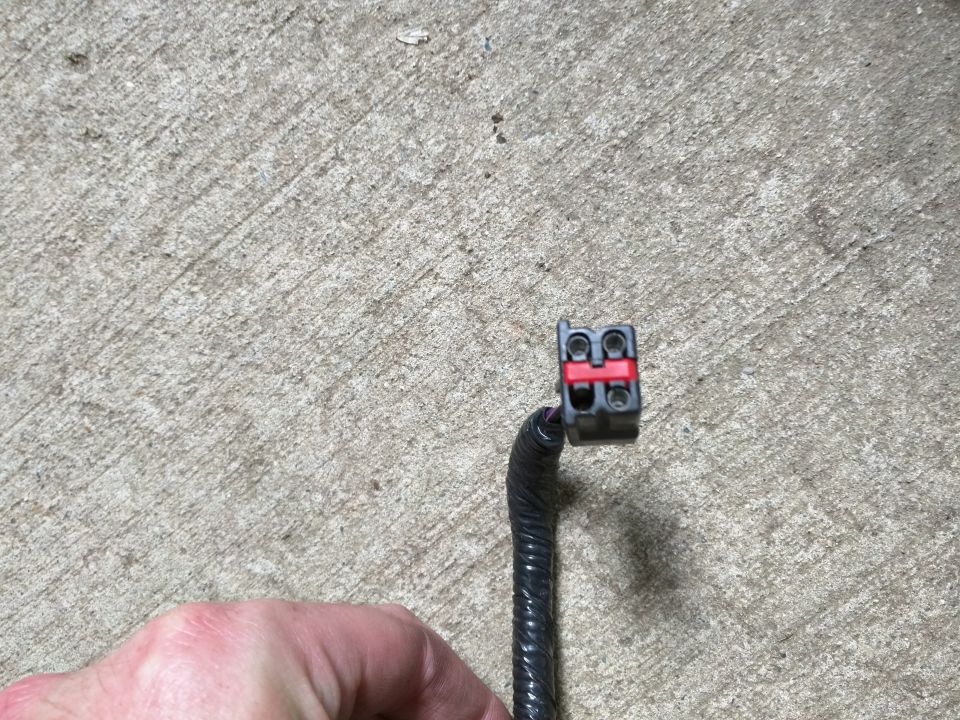 Black electrical connector with red locking tab on a black wire loom.