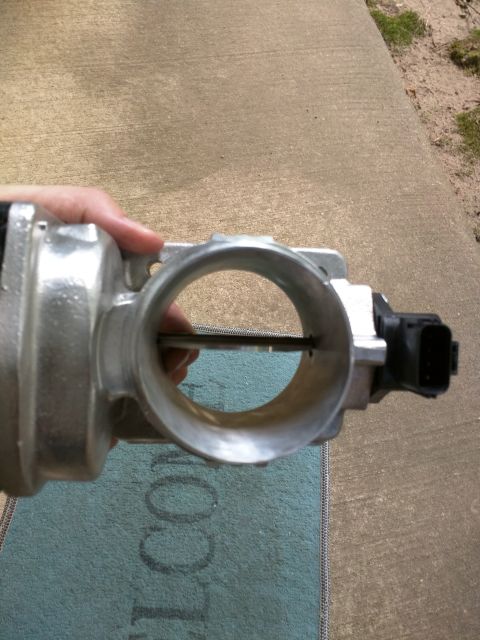 2007 Ford Crown Victoria - A person's hand holds a throttle body assembly, showing the internal butterfly valve. The part is silver aluminum with a black electrical c…