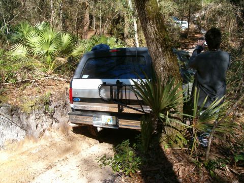 1991 Ford Bronco - A 1991 Ford Bronco navigates a wooded trail, with another vehicle visible further up the path.