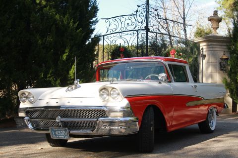 1958 Ford Ranchero - Two-tone 1957 Ford Ranchero parked outdoors near an ornate gate and trees.