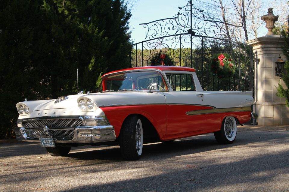 Red and white 1958 Ford Ranchero with whitewall tires parked by a gate