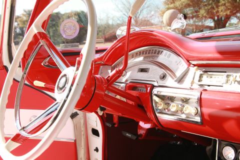1958 Ford Ranchero - The interior of a classic car features a two-tone steering wheel and a bright red dashboard with chrome accents.
