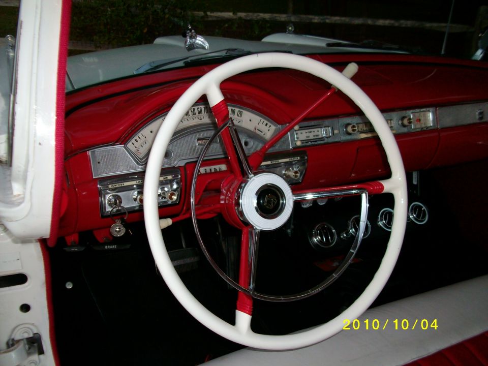 White steering wheel with red accents on a red dashboard. Radio and gauges visible