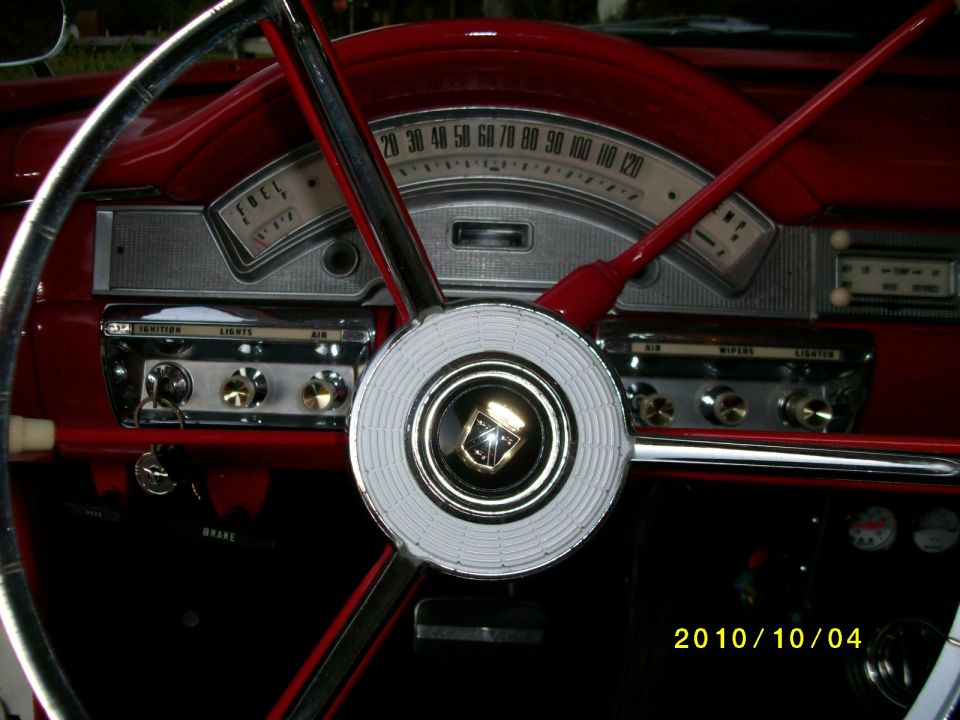 Red car interior with a white steering wheel and chrome accents. Dashboard has gauges and radio