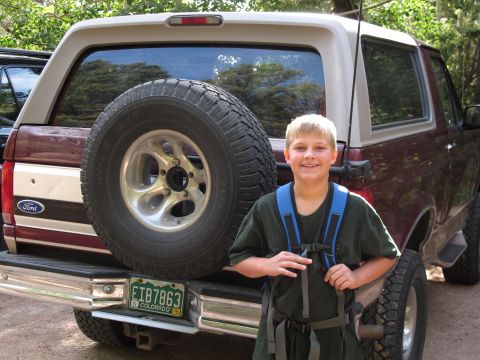 1996 Ford Bronco - A young boy stands next to a Ford Bronco, which has a spare tire mounted on its rear door.