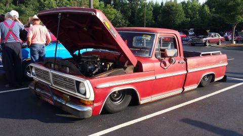 1976 Ford Ranchero - This red pickup truck features a distinctive chrome grille and a lowered stance, with its hood open to reveal the engine.