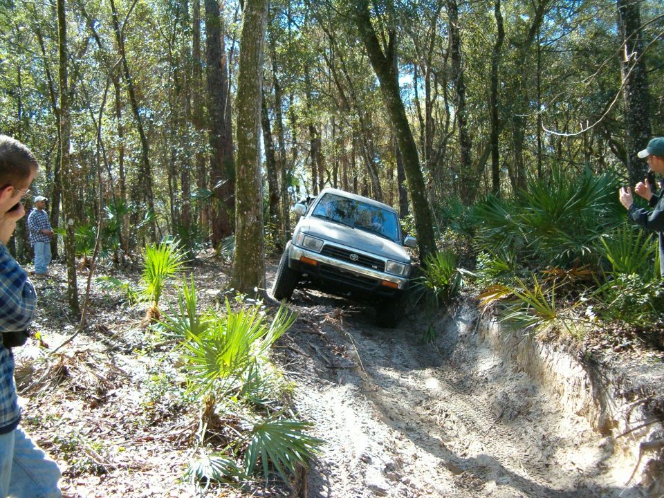 Silver SUV with a Toyota emblem on the grille, driving down a dirt path in a wooded area