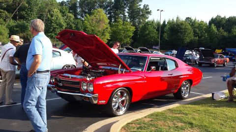 1976 Ford Ranchero - A bright red classic car with its hood up is the center of attention at an outdoor car show.