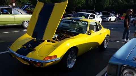 1976 Ford Ranchero - A yellow coupe with black racing stripes is displayed with its hood open at an outdoor car show.