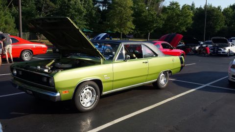 1976 Ford Ranchero - A lime green 1973 Plymouth Duster coupe is displayed with its hood open at an outdoor car show.
