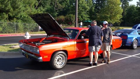 1976 Ford Ranchero - Two men look at an orange muscle car with its hood up at an outdoor car show.