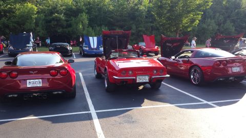 1976 Ford Ranchero - Multiple sports cars, including several red Corvettes, are displayed with their hoods open at a car show.
