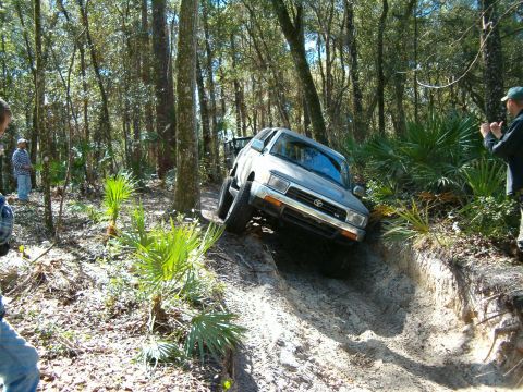1991 Ford Bronco - A silver 1996 Toyota 4Runner tackles a challenging off-road course, with spectators observing the action.