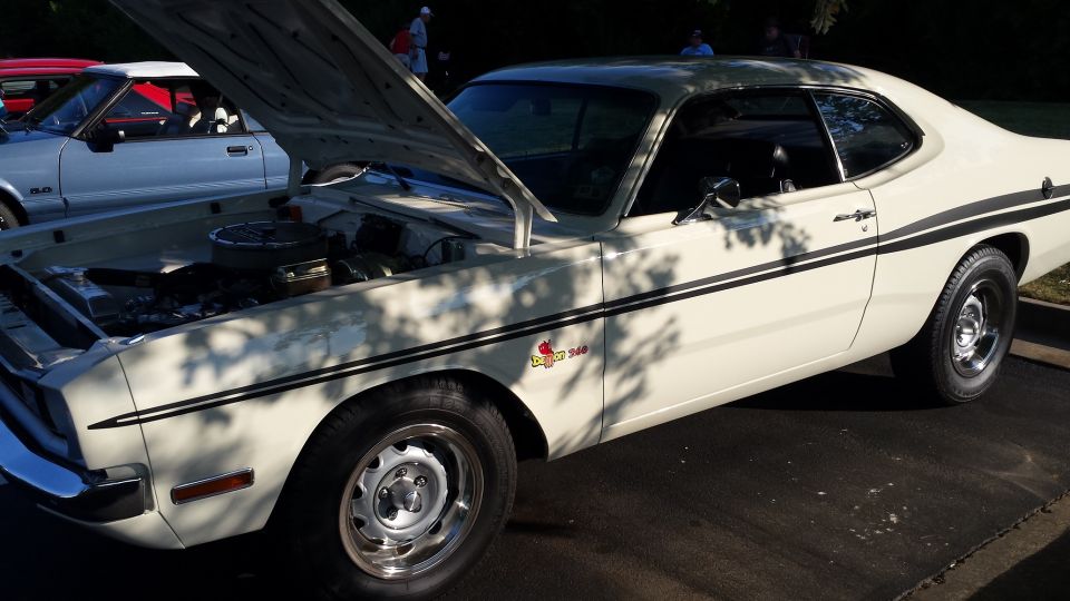 White coupe with black racing stripes and hood open, parked next to a silver car