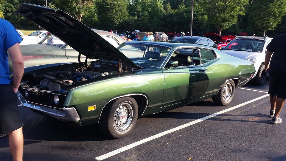 Green coupe with hood open, parked next to other cars