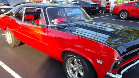 1976 Ford Ranchero - A red and black coupe with custom wheels is parked in a lot with other vehicles.