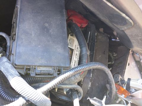 2007 Ford Crown Victoria - Close-up view of the engine bay, focusing on the battery and fuse box with visible wiring and some text on the battery label.