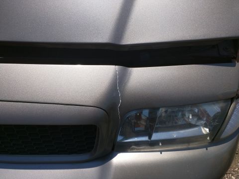 2007 Ford Crown Victoria - Damage to the front of a grey vehicle, showing a crack on the hood above the headlight.