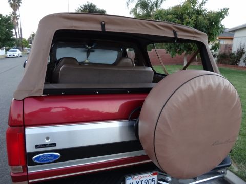 1994 Ford Bronco - The rear view of a red Ford Bronco, a tan soft top and a spare tire cover.