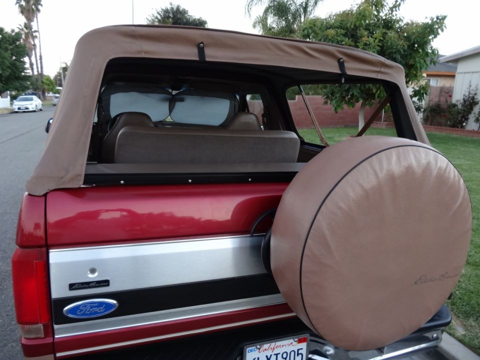 Red Ford Bronco with a tan soft top and a spare tire cover on the back