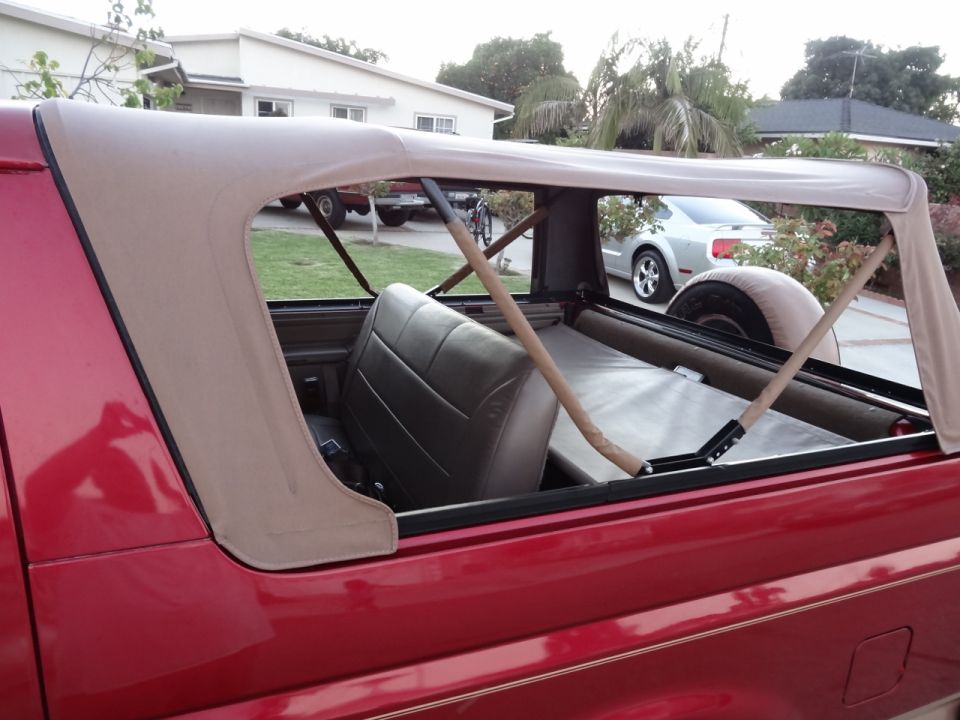 Red 1994 Ford Bronco with tan soft top, side view