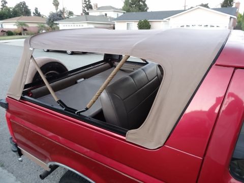 1994 Ford Bronco - This red Ford Bronco features a tan soft top and a rear passenger side view, with a spare tire visible.