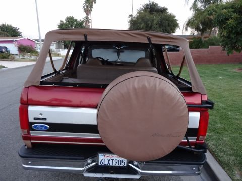 1994 Ford Bronco - Rear view of a red 1994 Ford Bronco a tan soft top and a spare tire cover.