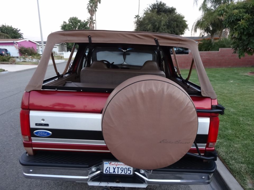 Red 1994 Ford Bronco rear view with tan soft top and spare tire cover