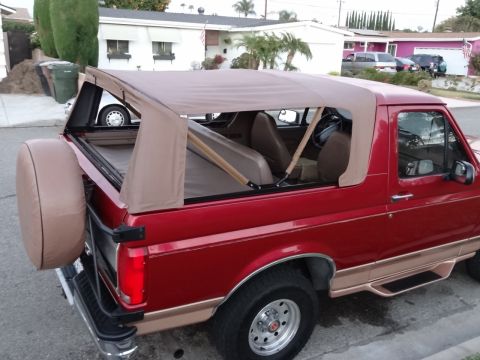 1994 Ford Bronco - This red Ford Bronco features a tan soft top and a spare tire mounted on the rear.