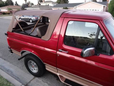 1994 Ford Bronco - Side view of a red 1994 Ford Bronco a tan soft top and two-tone trim.