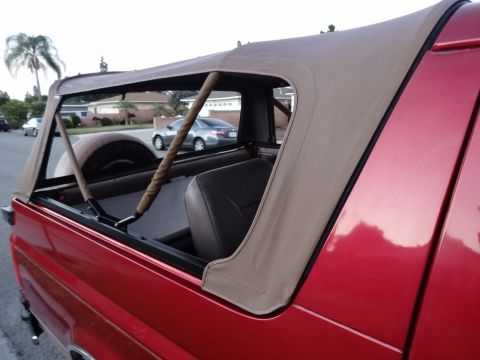 1994 Ford Bronco - The side view of a red SUV shows its tan soft top and interior details, with a residential street in the background.