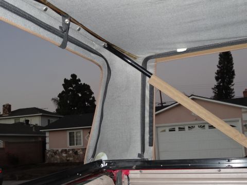 1994 Ford Bronco - The interior of a vehicle shows the frame and fabric of a soft top, with houses visible through the windows.