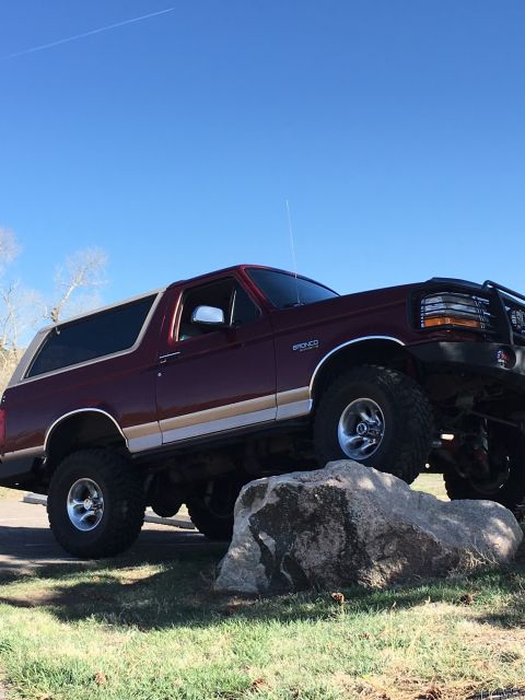 1996 Ford Bronco - A maroon 1996 Ford Bronco with tan trim is positioned on large rocks under a clear blue sky.