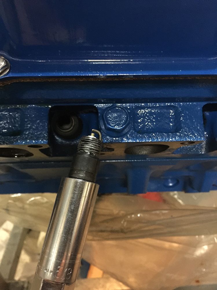 Spark plug with metal casing and threaded end, being inserted into a blue engine block