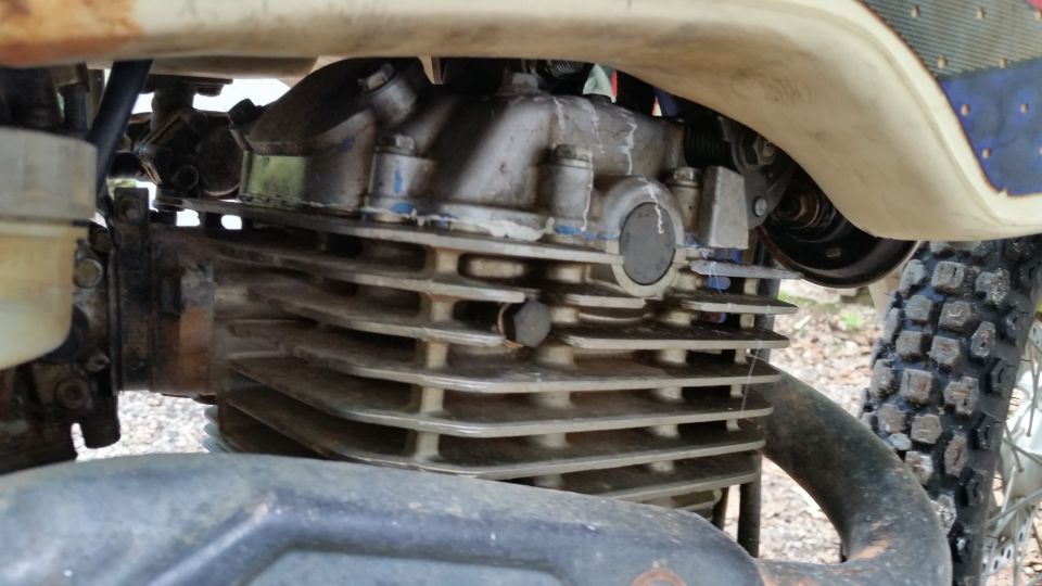Close-up of a motorcycle engine's cylinder head and fins. Text at bottom reads SUPERMOTORS.NET