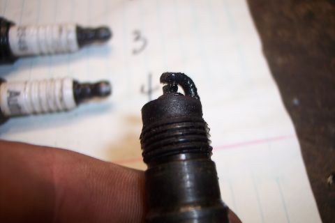 1990 Ford Bronco - A fouled spark plug is shown in detail, with two other spark plugs out of focus behind it.
