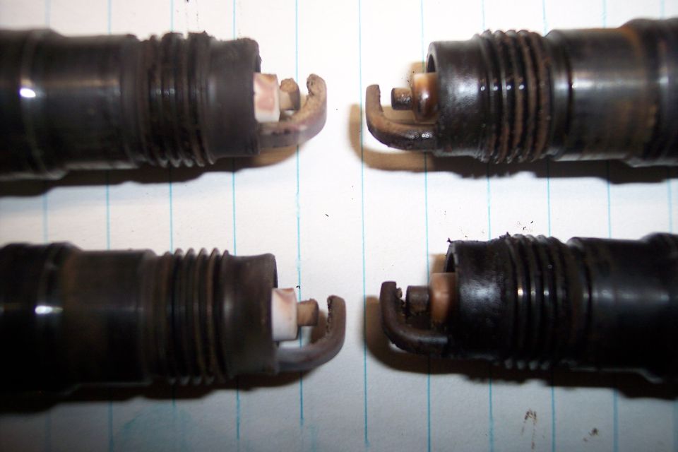 Four used spark plugs on lined paper, two in focus at top, two at bottom