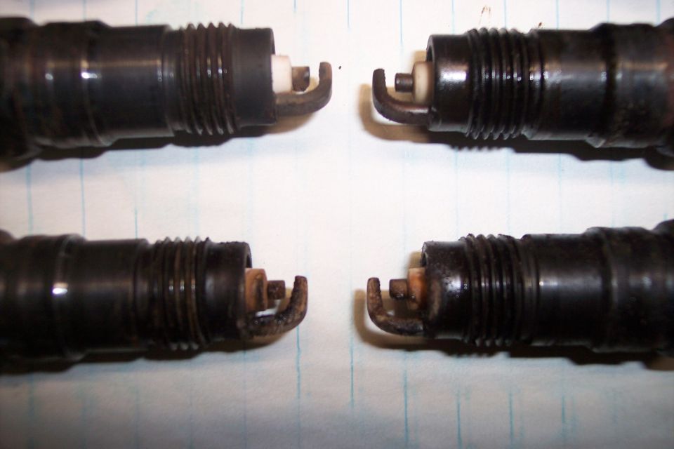 Four used spark plugs, two in the top row and two in the bottom row