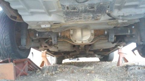 2004 Ford Crown Victoria - The underside of a vehicle is shown, supported by jack stands, revealing the rear axle and suspension components.