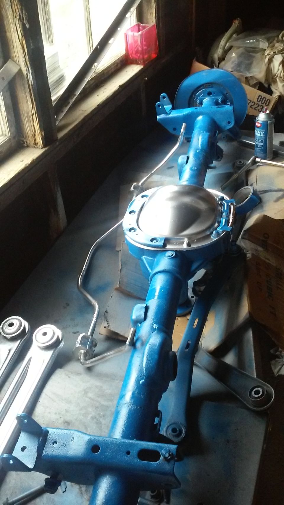 Blue painted rear axle assembly with brake components and suspension links on a workbench
