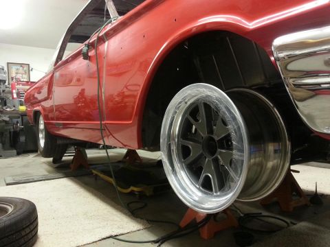 1964 Ford Fairlane - A classic red car is elevated on jack stands in a workshop, revealing its undercarriage and a custom wheel.