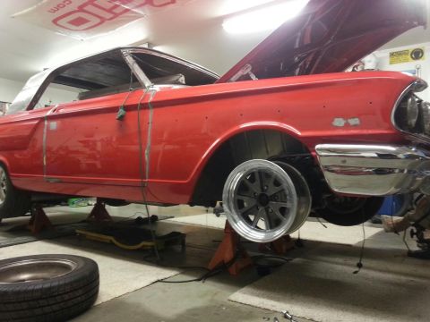 1964 Ford Fairlane - A red 1964 Ford Fairlane coupe is shown from the side, elevated on jack stands with its hood open, indicating it is in a state of repair.