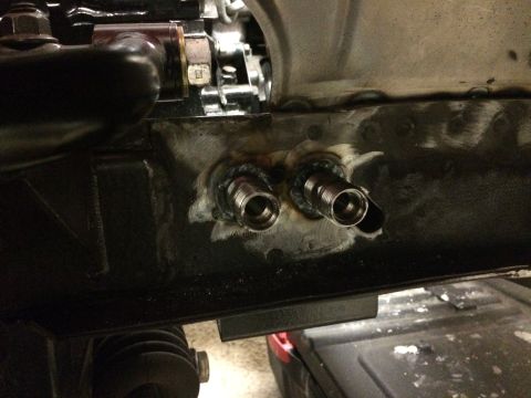 1964 Ford Fairlane - Two threaded fittings are welded onto a black metal bracket, likely for a fluid or air line connection. The bracket appears to be part of a…