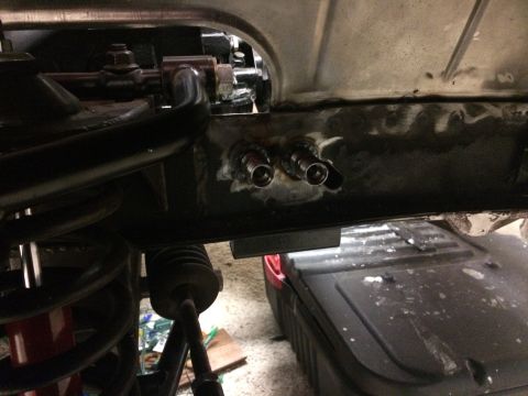 1964 Ford Fairlane - Close-up view of the underside of a vehicle, showing a black metal frame with two metal fittings welded onto it. A suspension component wit…