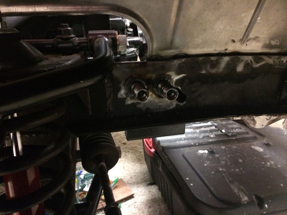 Underside of a vehicle frame with welded fittings and suspension components.