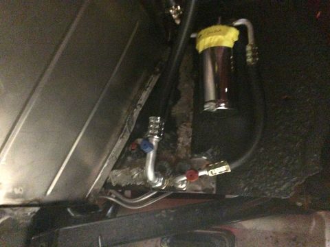 1964 Ford Fairlane - A close-up view of a custom fuel filter installation under a vehicle, featuring a chrome canister with yellow tape and various metal lines…