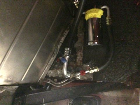 1964 Ford Fairlane - A close-up view shows a chrome fuel filter with a yellow cap, connected by hoses and valves to a vehicle's undercarriage. The filter appear…